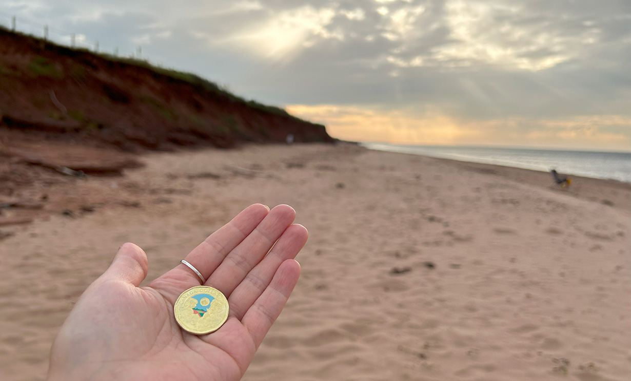 L. M. Montgomery commemorative circulation coin on red sand beach