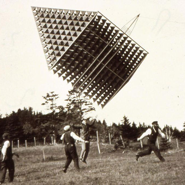 Photo d’un cerf-volant tétraédrique entouré de personnes dans un champ.